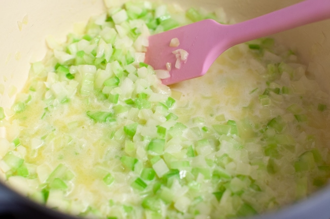 Cooking onion and celery with butter in a pot with a pink rubber spatula