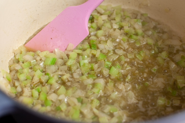 Cooking onion and celery with butter in a pot with a pink rubber spatula