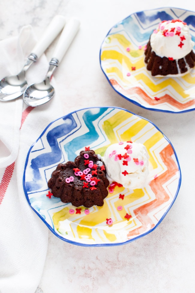 heart shaped chocolate cake with vanilla ice cream on a plate with spoons another plate in the background