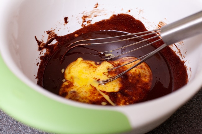 beaten eggs in a mixing bowl with melted chocolate and a whisk