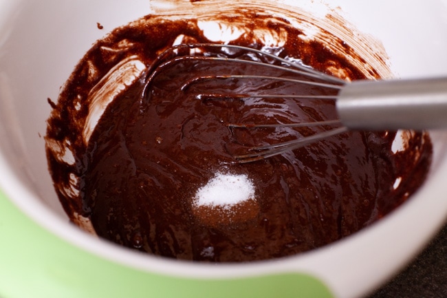 salt, espresso powder and a whisk on top of melted chocolate in a mixing bowl