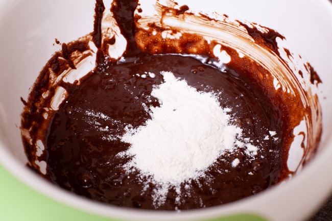 flour on top of a chocolate mixture in a mixing bowl