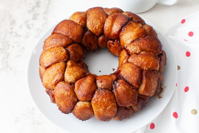 monkey bread on a plate with a napkin and a pitcher with frosting in the background