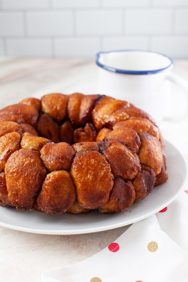 monkey bread on a plate with a napkin and a pitcher with frosting in the background
