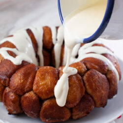 monkey bread on a plate with a napkin and a pitcher with pouring frosting