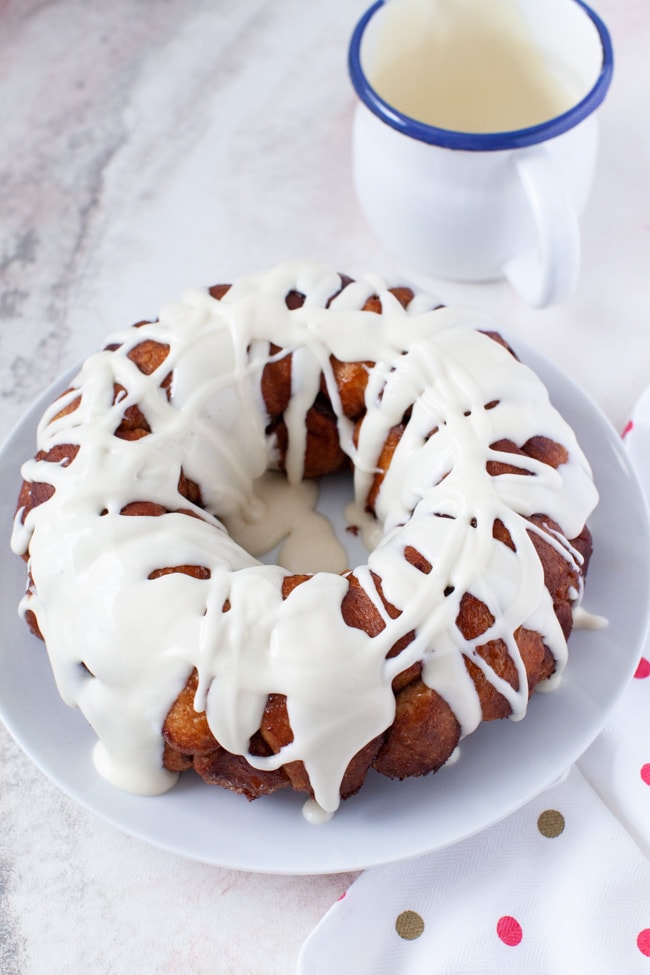 monkey bread on a plate with cream cheese frosting on top and a pitcher with frosting in the background