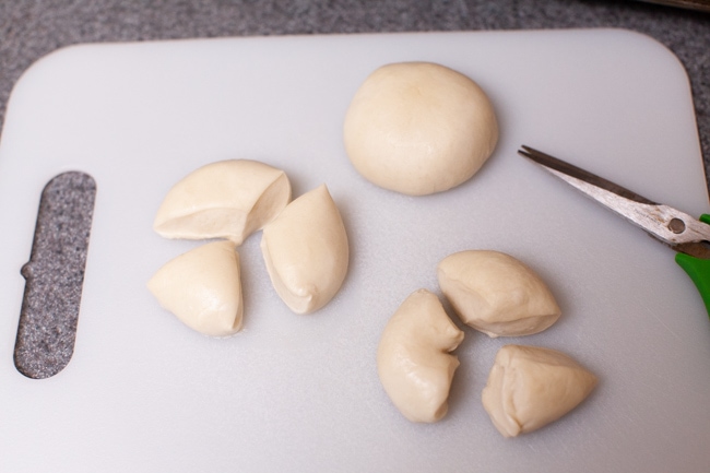 cut pieces of yeast rolls on a cutting board with a pair of kitchen shears