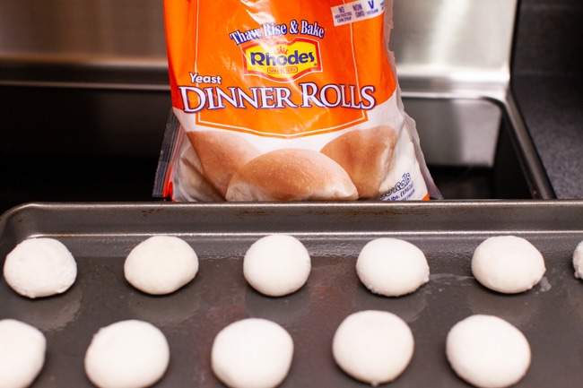 frozen yeast dinner rolls on a baking dish with a bag of Rhodes Dinner Rolls behind it