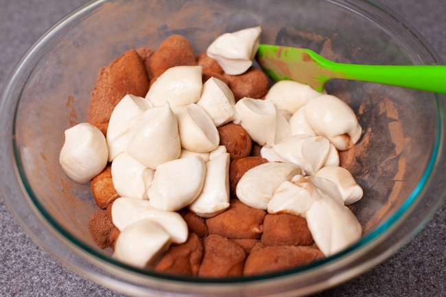 dough balls that have been rolled in a cinnamon and sugar mixture sitting in a glass bowl.