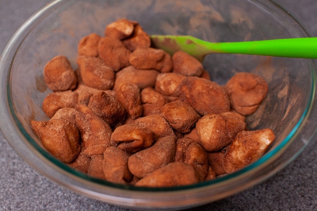 dough balls that have been rolled in a cinnamon and sugar mixture sitting in a glass bowl.