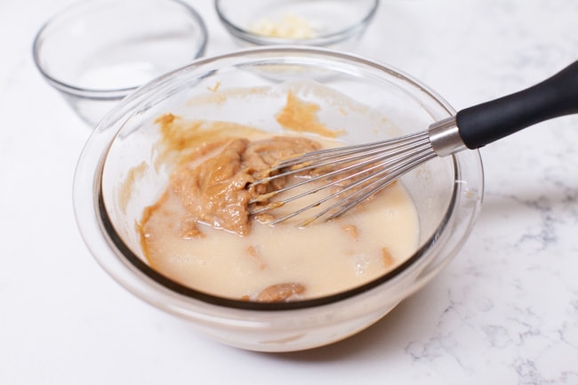 making peanut sauce in a glass mixing bowl with a whisk