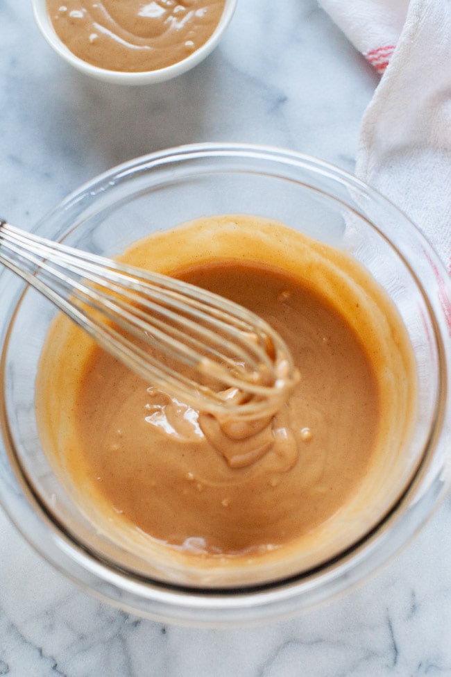 peanut sauce in a glass bowl with a whisk over the bowl