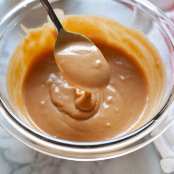 peanut sauce on a spoon over a glass bowl with a napkin in the background