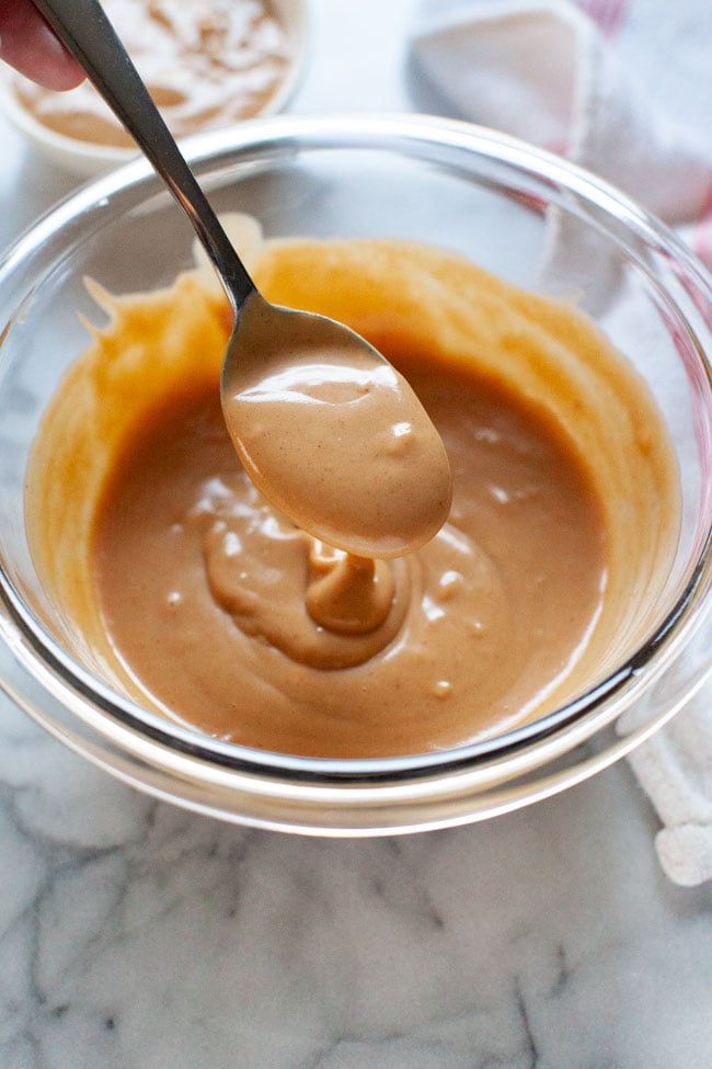 peanut sauce on a spoon over a glass bowl with a napkin in the background