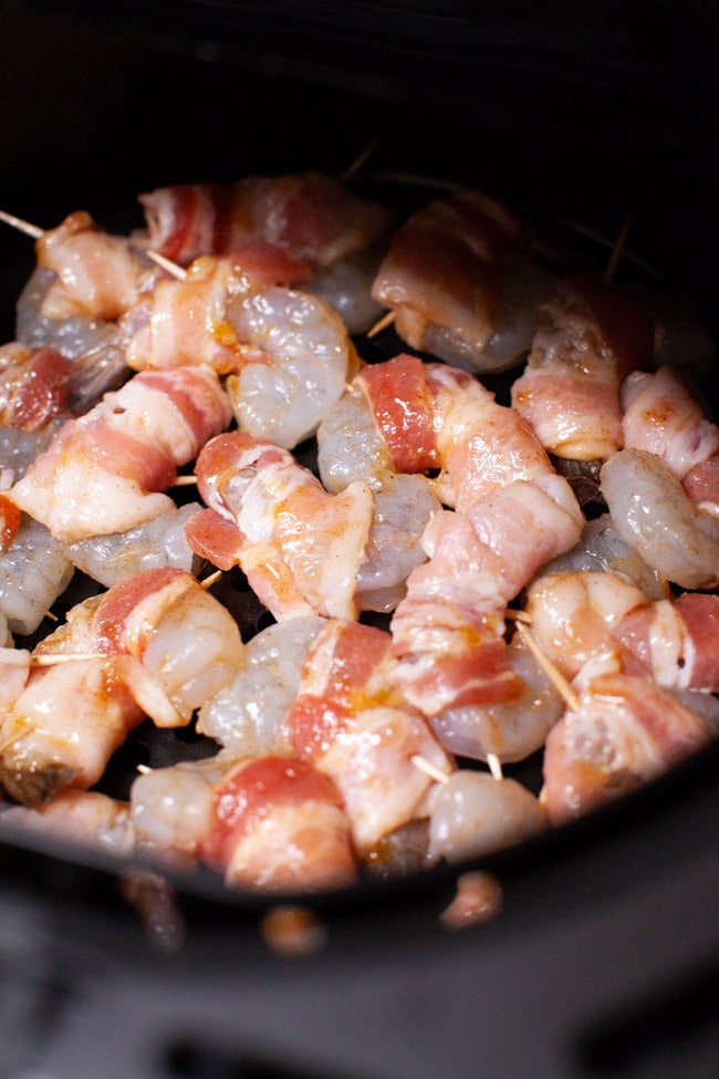 raw bacon wrapped shrimp in the basket of an air fryer
