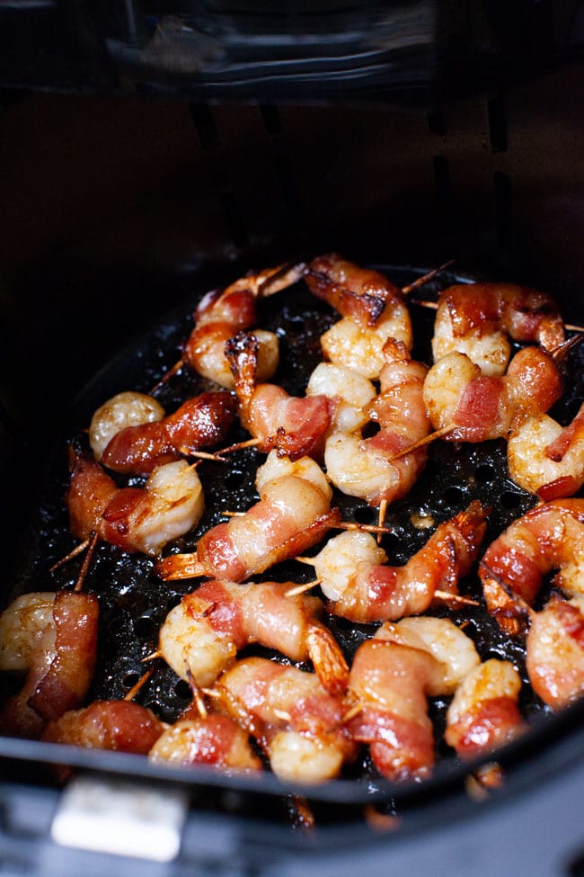 cooked shrimp wrapped in bacon with toothpicks pushed through in the basket of an air fryer