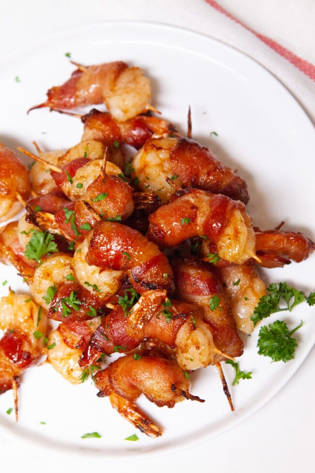 bacon wrapped shrimp on a white plate sprinkled with parsley