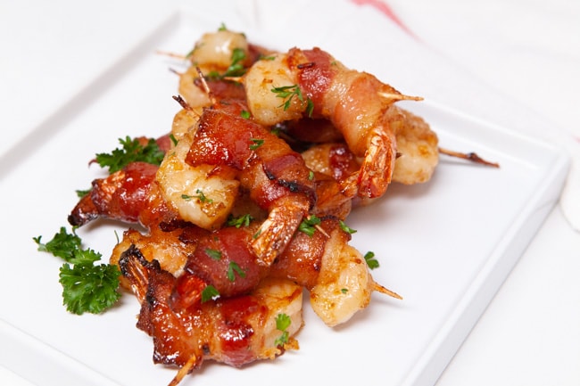 bacon wrapped shrimp on a white plate sprinkled with parsley