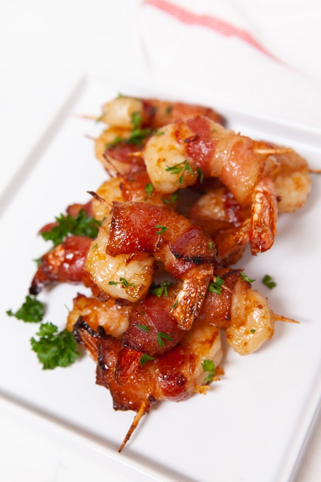 bacon wrapped shrimp on a white plate sprinkled with parsley