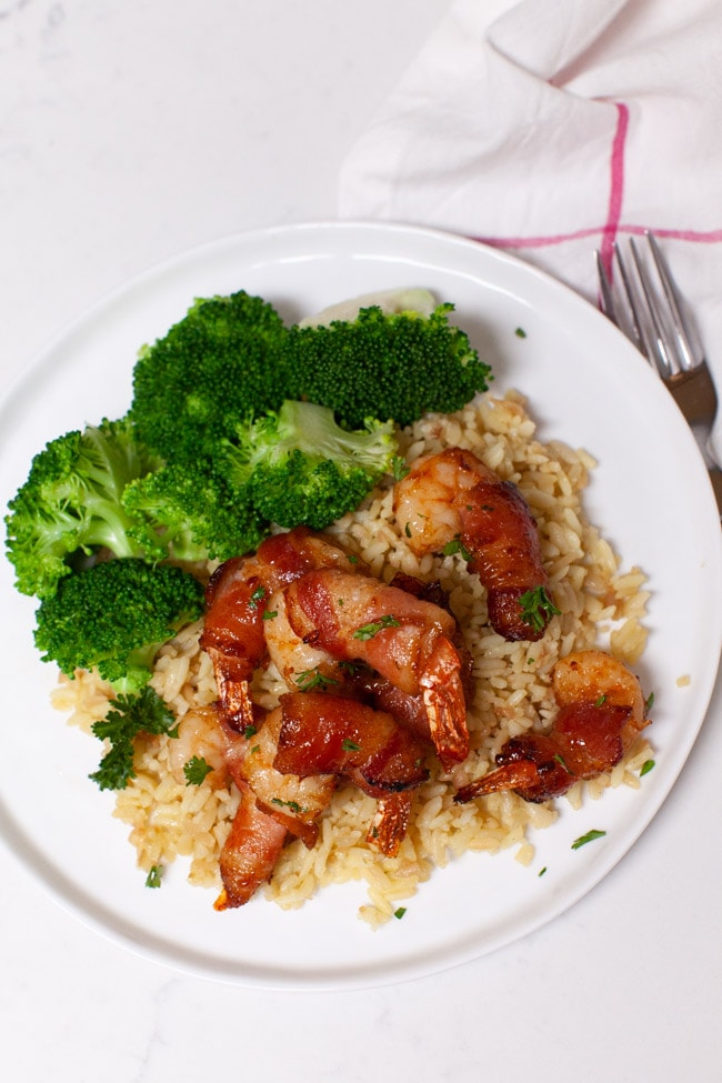 overhead view of bacon wrapped shrimp served on a bed of rice next to a side of broccoli