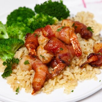 bacon wrapped shrimp on a plate of rice next to broccoli
