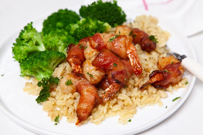 bacon wrapped shrimp on a plate of rice next to broccoli