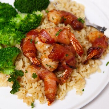 shrimp wrapped in bacon con top of rice next to steamed broccoli on a white plate