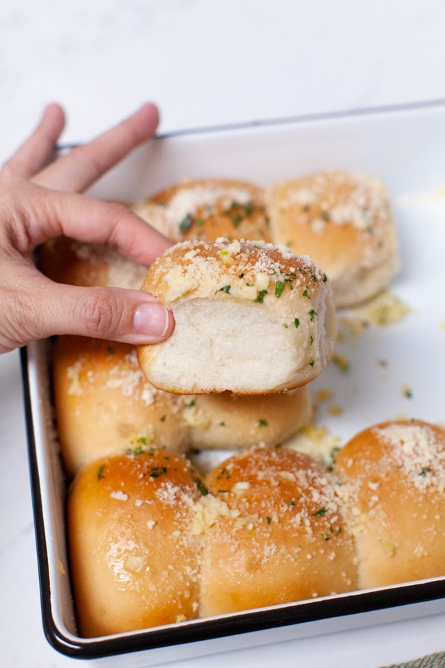 a hand holding a parmesan garlic roll with garlic rolls in a baking dish in the background