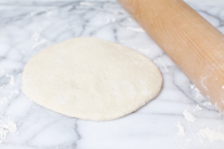 pizza dough rolled out on a marble slab with a rolling pin