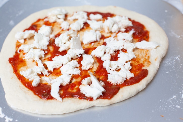 pizza on a pizza peel with tomato sauce and mozzarella cheese