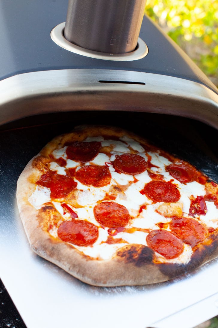 Pepperoni Pizza on a pizza peel coming out of a Ooni pizza oven