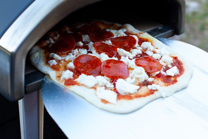 Pepperoni Pizza on a pizza peel coming out of a Ooni pizza oven