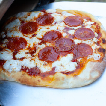 Pepperoni Pizza on a pizza peel coming out of a Ooni pizza oven