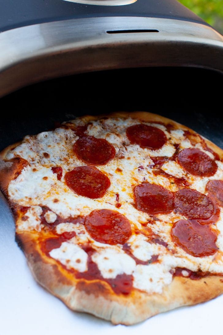 Pepperoni Pizza on a pizza peel coming out of a Ooni pizza oven