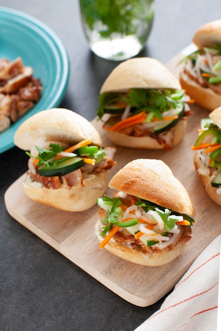 chicken banh mi sliders on a wooden board with a plate of chicken in the background