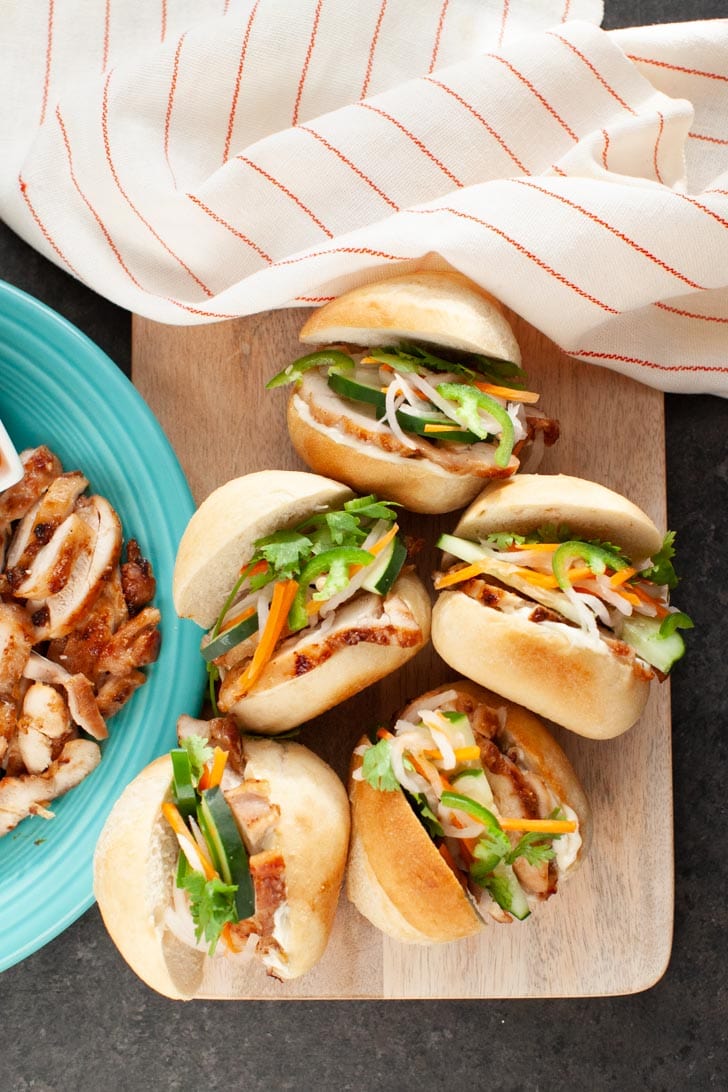 chicken banh mi sliders on a wooden board with a plate of chicken on the left side