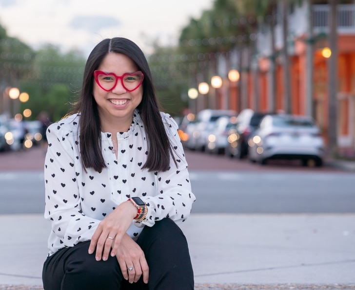 Julie Deily sitting on a sidewalk with cars in the background