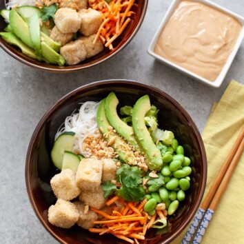brown bowl with tofu, noodles, edamame, carrots and avocado with another bowl in the background